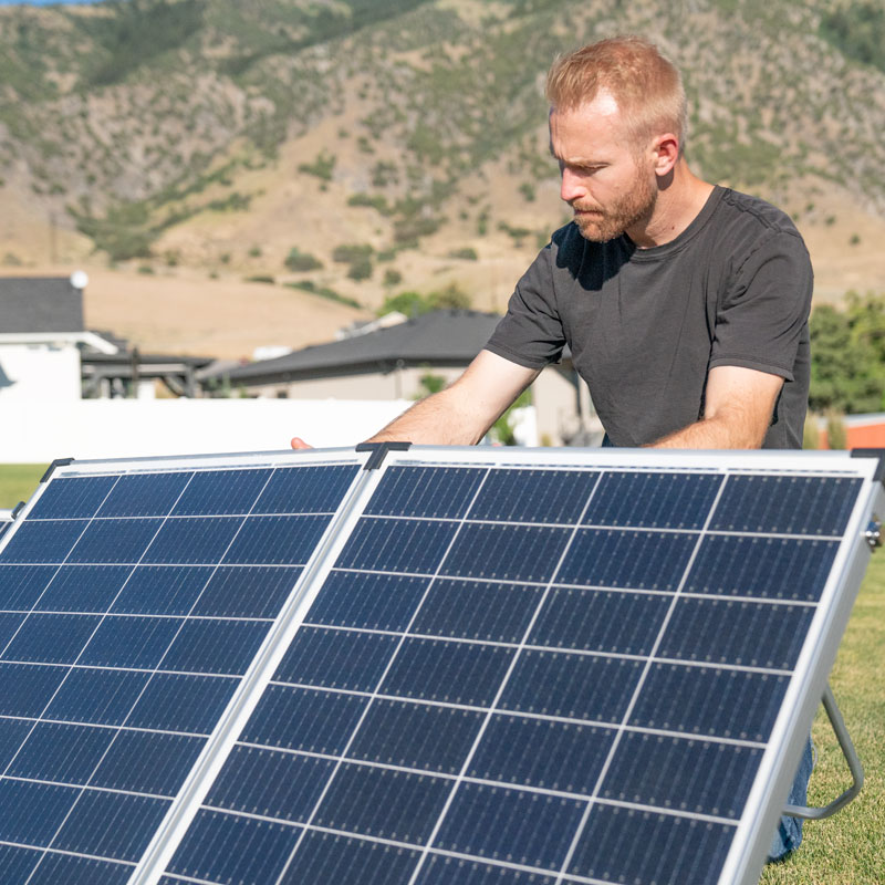 Man setting up foldable, portable solar panels on a warm, sunshine day in his backyard. 