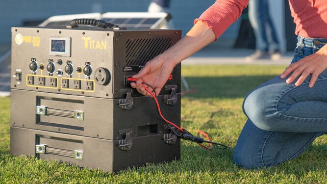 A woman connects solar power wires to the Titan solar generator with two lithium ion expansion batteries.