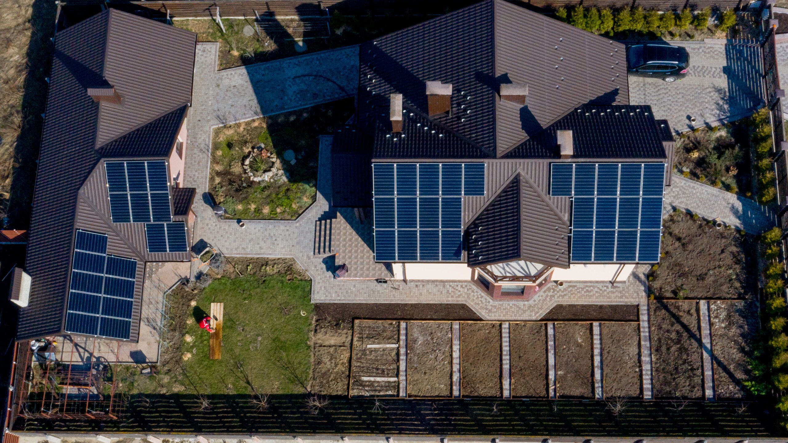 Aerial top view of a house with paved yard with green grass lawn with concrete foundation floor that has solar panels covering some of the roof. 