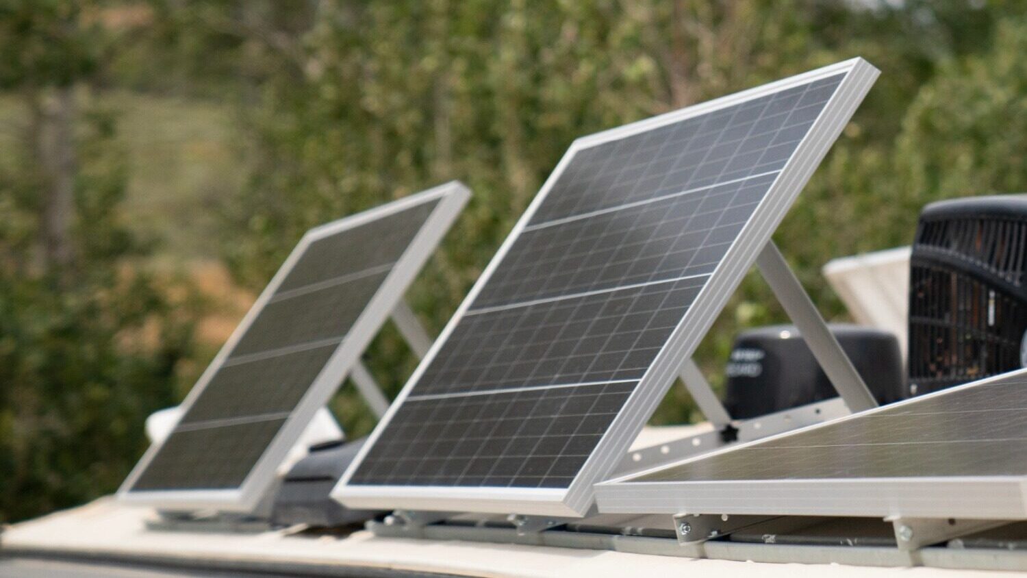 Two 100-watt solar panels on the top of an RV in the woods on a sunny day. 
